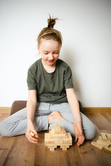 girl with funny hairstyle playing on the floor with a wooden constructor. Board Games. leisure for children