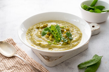 Green cream soup with green fresh peas on bright background. Healthy, vegan food