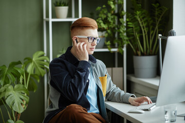 Portrait of trendy young businessman using computer while working at desk in green office