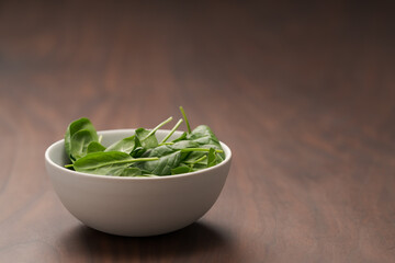 Fresh spinach leaves in white bowl on walnut wood table