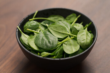 Fresh spinach leaves in black bowl on walnut wood table