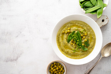 Green cream soup with green fresh peas on bright background. Healthy, vegan food