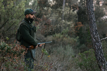 Young hunter holding his shotgun in middle of nature looking down