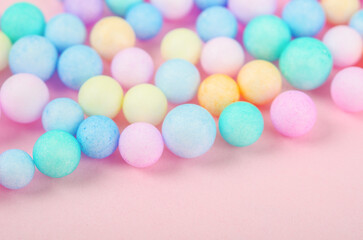 Foam beads of various colors brightly colored on pink pastel background with empty space.