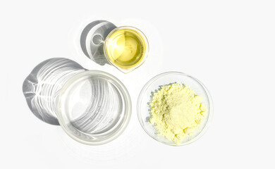 Cosmetic chemicals ingredient on white laboratory table. Sulfur Powder in Chemical Watch Glass and Poly Aluminium chloride liquid in beaker. Top View