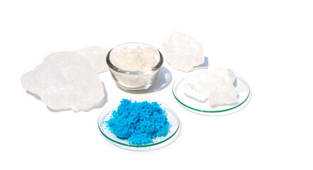 Closeup inorganic chemical on white laboratory table. Copper(II) sulfate in Chemical Watch Glass. Alum Crystal and Flake salt were placed further away.