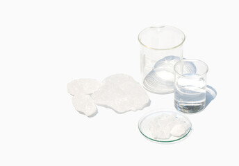 Alum Crystal in Chemical Watch Glass placed next to the beaker containing transparent chemicals, free of odor on laboratory table.