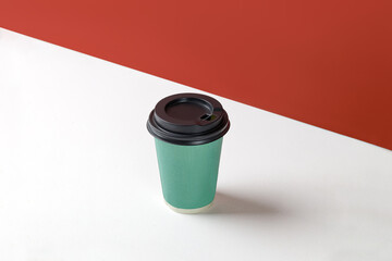 Green paper cup with coffee on white background and red wall. Disposable paper cup closeup. Blank space for text, mockup