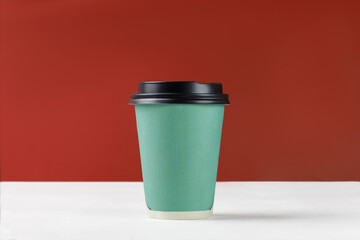 Green paper cup with coffee on white background and red wall. Disposable paper cup closeup. Blank space for text, mockup