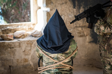 A caucasian woman in an army uniform holds a hostage with a bag on her head at the sight of a machine gun. 