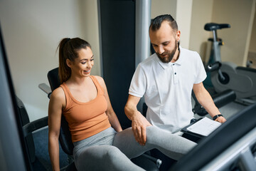 Fototapeta na wymiar Personal trainer assists athletic woman with exercising on leg press machine in health club.