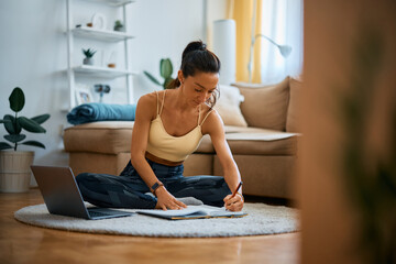 Fototapeta na wymiar Female fitness instructor taking notes while using laptop at home.