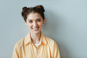 Minimal portrait of cheerful young woman with genuine smile looking at camera against blue wall,...