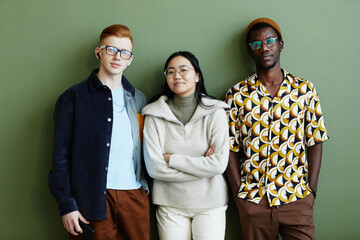 Minimal portrait of diverse creative team looking at camera while standing against green wall in...