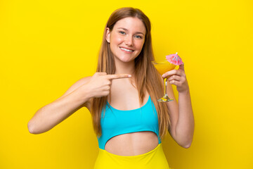Young caucasian woman holding a cocktail isolated on yellow background and pointing it