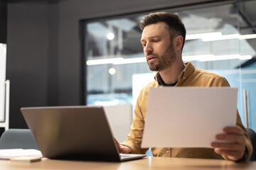 Businessman Using Laptop Holding Paper Working At Workplace In Office