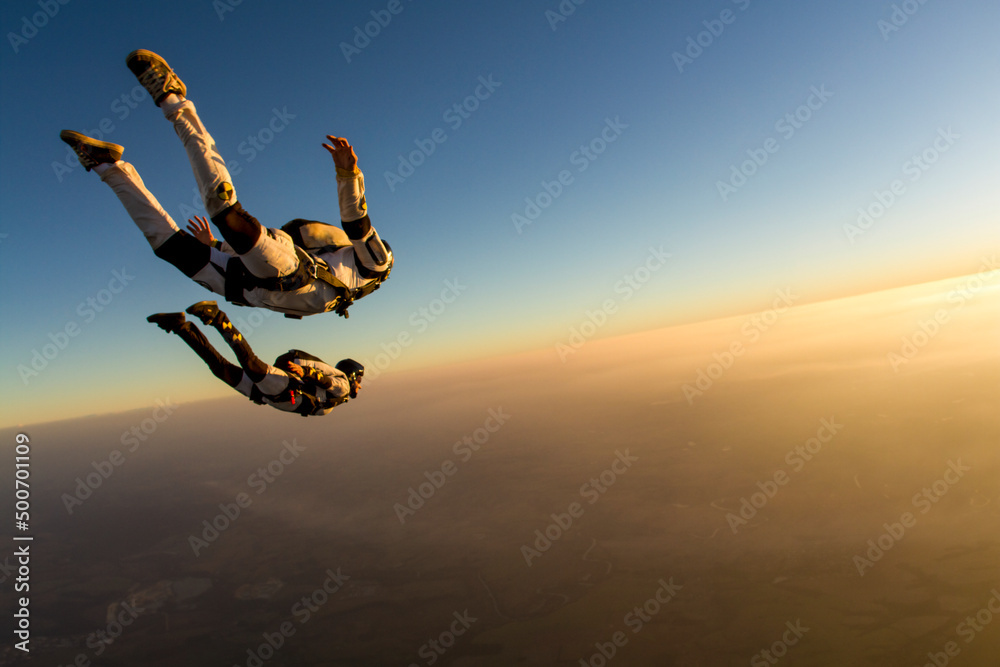 Wall mural Skydiving couple in freefall at sunset, togetherness concept