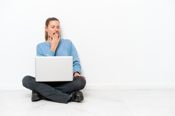 Young woman with a laptop sitting on the floor yawning and covering wide open mouth with hand