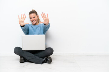 Young woman with a laptop sitting on the floor counting ten with fingers