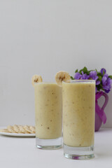 banana smoothie in a clear glass on a white background with purple flowers