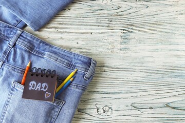 Father's day, pencils and notepad with congratulations to dad in jeans pocket on a wooden...