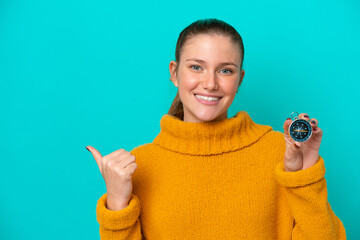 Young caucasian woman holding compass isolated on blue background pointing to the side to present a product © luismolinero