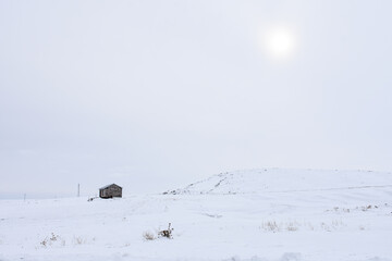 a small shack in the middle of wild winter nature and sun is barely seem
