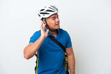 Young caucasian man with thermal backpack isolated on white background listening to something by putting hand on the ear