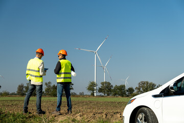 Wind generators maintained by professional technicians. Workers check efficiency of contemporary windmills via tablet against clear blue sky