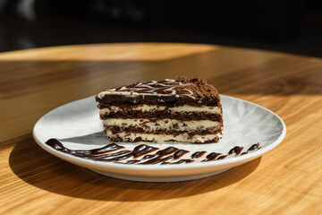 A piece of cake on a white plate decorated with cream. Baking coffee in a cafe on a wooden table. Isolated from background. Chocolate cake
