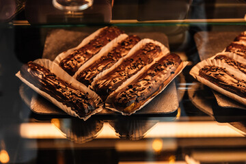 Tasty chocolate eclairs on window shop in cafe. Delicious pastries for coffee. Eclairs on dark background under the light