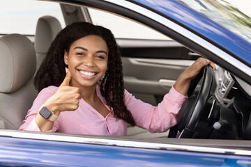 Happy black woman sitting in car showing like gesture