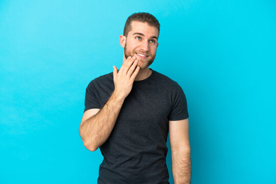 Young handsome caucasian man isolated on blue background looking up while smiling