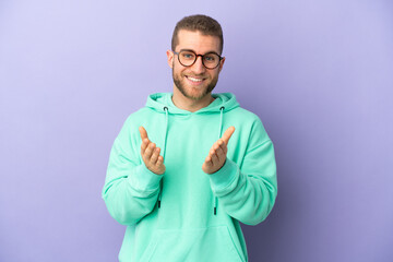 Young handsome caucasian man isolated on purple background applauding after presentation in a conference