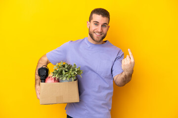 Young caucasian making a move while picking up a box full of things isolated on yellow background...