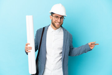 Young architect man with helmet and holding blueprints over isolated background pointing finger to...