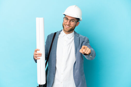 Young architect man with helmet and holding blueprints over isolated background pointing front with happy expression