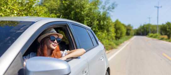 Woman with ginger red hair wearing sunglasses driving car in solo weekend getaway vacation trip...