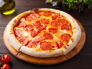Traditional Italian pepperoni pizza with salami and cheese on a dark brown wooden background. Top view with space to copy. Olive oil, cherry, lettuce. Menu of cafes, pizzerias, restaurants. Close up.