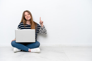 Young caucasian woman with a laptop sitting on the floor isolated on white background showing and lifting a finger in sign of the best