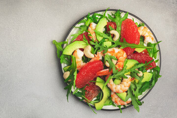 Delicious salad with shrimps, avocado, grapefruit, arugula and cashews. Grey stone table background, top view, negative space