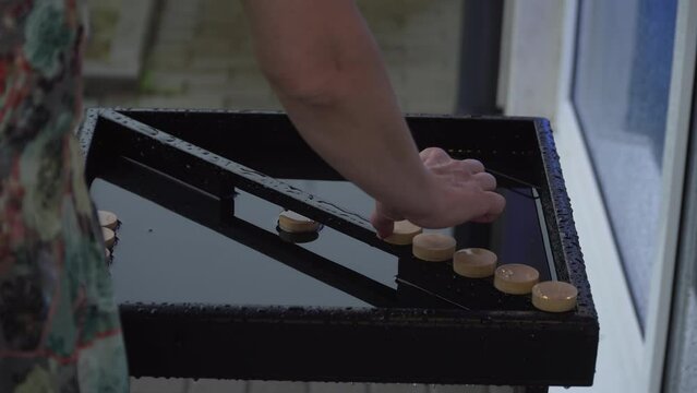 Woman hand takes out round chips from wooden board game flooded with rain. Person keeps the property. Lady shakes off water and lays toy blocks on center bar to dry. Flood after downpour in city.