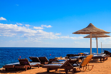 Sun umbrellas and chaise lounges on tropical beach. Concept of rest, relaxation, holidays, resort