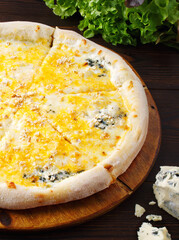 Pizza with 4 cheeses on a wooden background. Cream sauce, mozzarella cheese, Door blue cheese, Maasdam cheese, parmesan cheese. Menu of cafes, pizzeria, restaurant. Close up. Copy space. Fresh dorblu.