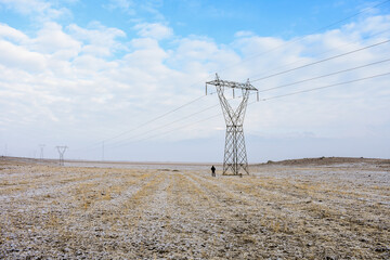 man walking near high voltage line electric pole in field, winter season