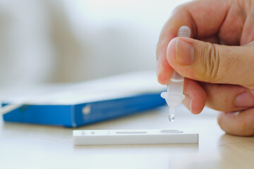 CLoseup hand using rapid antigen test kit (ATK) for self test at home. Dropping sample fluid on test kit. Pandemic of disease, covid-19, coronavirus