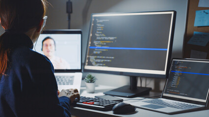 Asian woman developer programmer, software engineer, IT technical support center talking with team via video call. Working on computer overtime to check coding in bugging system. Back view