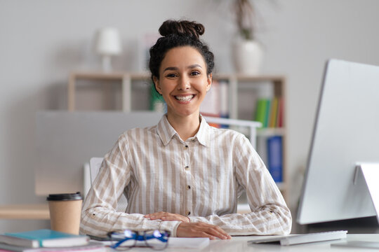 Portrait of cheerful female manager sitting at workplace at contemporary office and smiling at camera