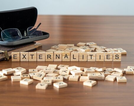 externalities word or concept represented by wooden letter tiles on a wooden table with glasses and a book