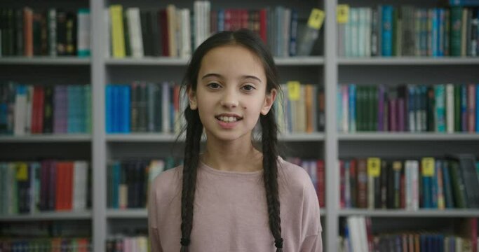 Asian girl with braids looks in camera smiling in library